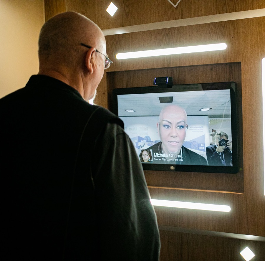 A museum visitor watches a screen that transforms his face into Michelle Obama's at a deepfake exhibition.