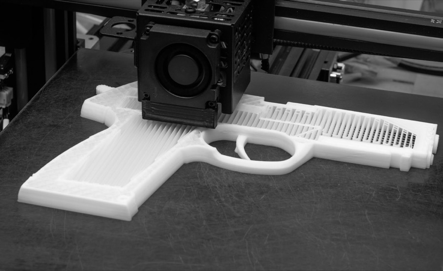 A 3D printer building a white plastic handgun.